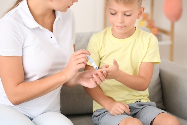 Mère prenant un échantillon de sang de fils diabétique à la maison