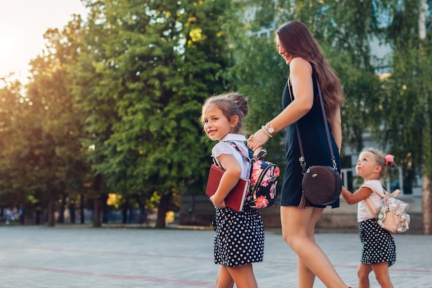 Mère rencontrant des enfants filles après les cours à l'extérieur de l'école primaire La famille rentre à la maison avec des livres. Retour à l'école. Éducation