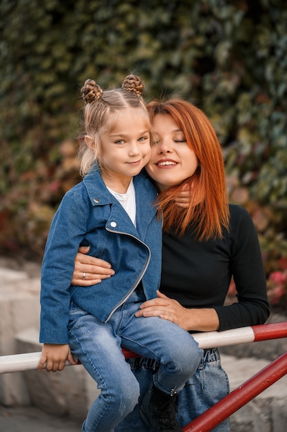 Une mère rousse élégante et sa fille parlent chaleureusement. Enfant heureux et sa maman dans la rue. Mère célibataire réussie avec sa fille pour une promenade. Relation familiale chaleureuse