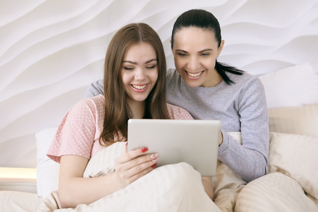 Mère avec sa fille adolescente regardant un film sur l'écran du tablet pc au lit