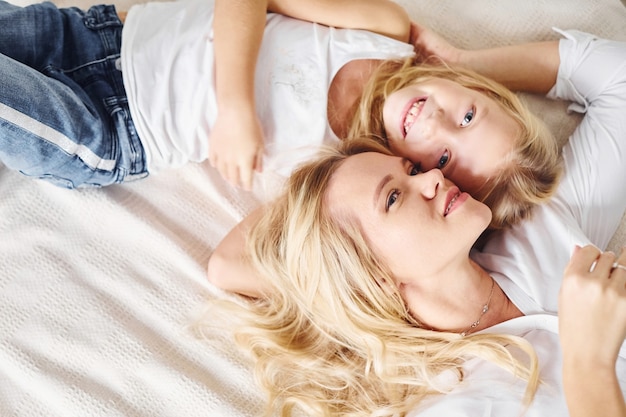 Mère avec sa fille allongée ensemble sur le lit blanc.