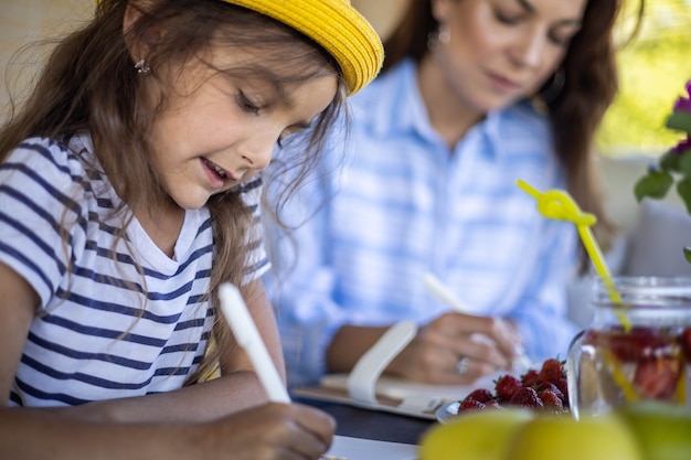 Une mère et sa fille ciblées à la recherche d'un cahier d'horaire en papier se relaxant sur une terrasse extérieure