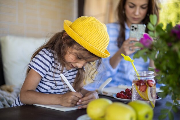 Une mère et sa fille ciblées à la recherche d'un cahier d'horaire en papier se relaxant sur une terrasse extérieure