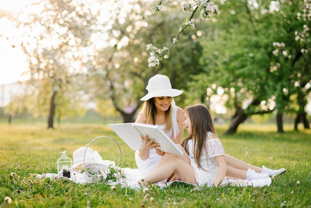 Une mère et sa fille dans le jardin printanier sur un plaid feuilletent et parcourent un livre avec des photos d'une séance photo de famille Rappelez-vous les moments importants de la vie dans l'album photo