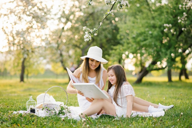 Une Mère Et Sa Fille Dans Le Jardin De Printemps Sur Un Plaid Feuilletent Et Regardent à Travers Un Livre