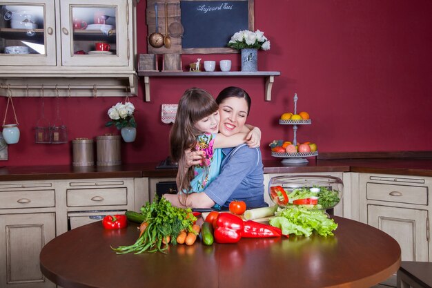 Une mère et sa fille heureuses aiment préparer et prendre des repas sains ensemble dans leur cuisine. ils préparent une salade de légumes et s'amusent ensemble. maman s'occupe de sa fille et apprend à cuisiner.