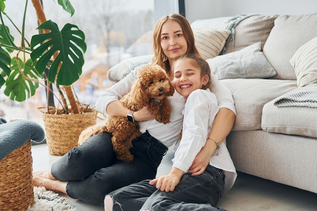 Mère avec sa fille jouant avec un chien Le mignon petit chiot caniche est à l'intérieur dans la chambre domestique moderne