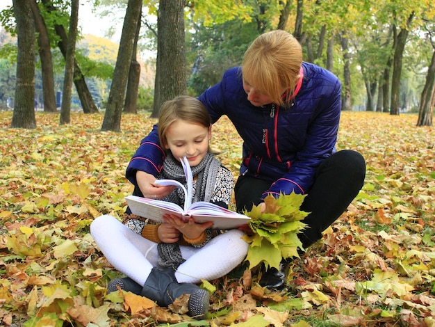mère et sa fille lisent un livre dans le parc de la ville d'automne