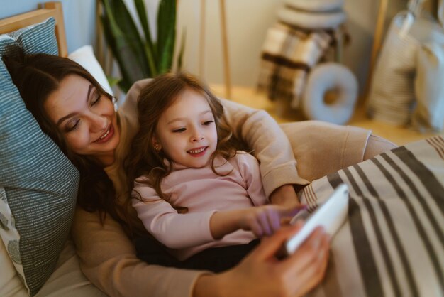 Une mère et sa fille sont allongées sur un canapé et regardent une tablette.