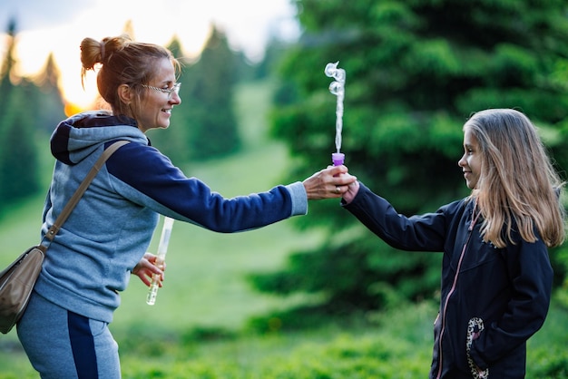 Mère et sa fille soufflent des bulles de savon dans la forêt d'épicéas lors d'une promenade