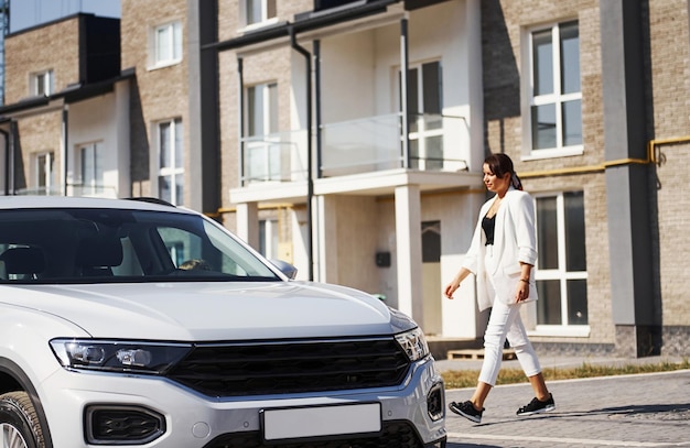 Mère avec sa fille en uniforme scolaire à l'extérieur près d'une voiture blanche.