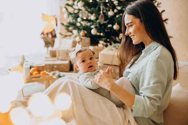 Mère avec sa petite fille assise près de l'arbre de Noël