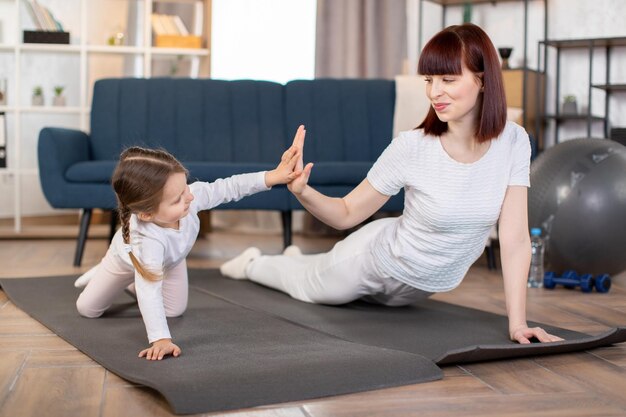 Mère et sa petite fille mignonne faisant des exercices de pompes sur un tapis de yoga dans le salon à la maison