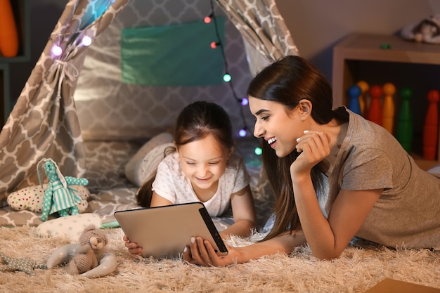 Mère et sa petite fille avec tablette à la maison en soirée