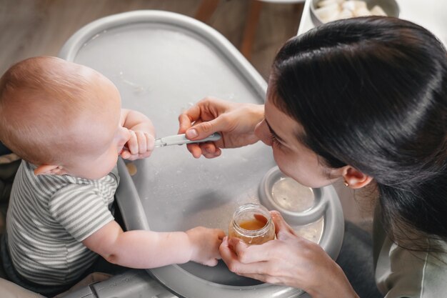 Mère se nourrissant de légumes ou de fruits pur bébé sur chaise haute