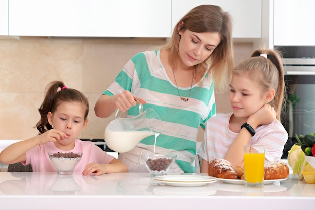 Mère servant le petit déjeuner à ses deux filles à une table dans la cuisine, concept de mère célibataire heureuse