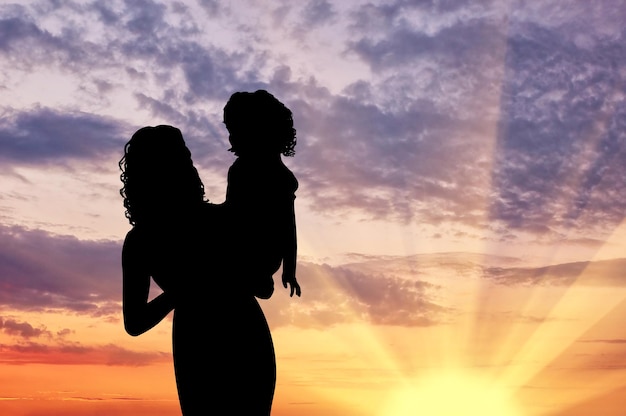 Mère de silhouette avec un enfant au coucher du soleil