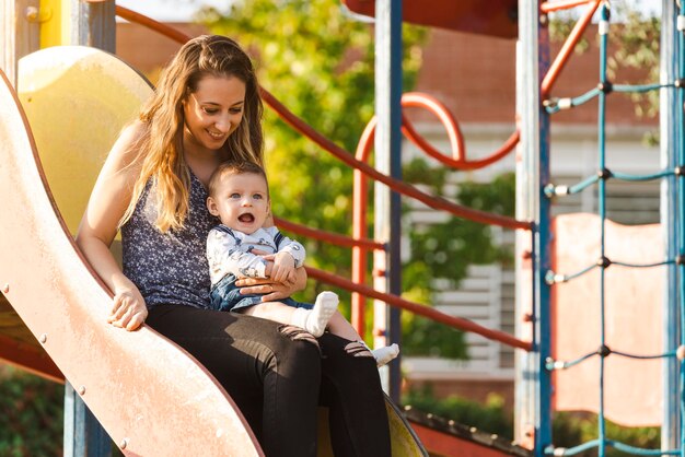 Mère avec son bébé sur un toboggan du parc au coucher du soleil