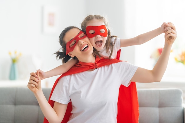 Mère et son enfant jouant ensemble Fille et maman en costume de super-héros Maman et enfant s'amusant