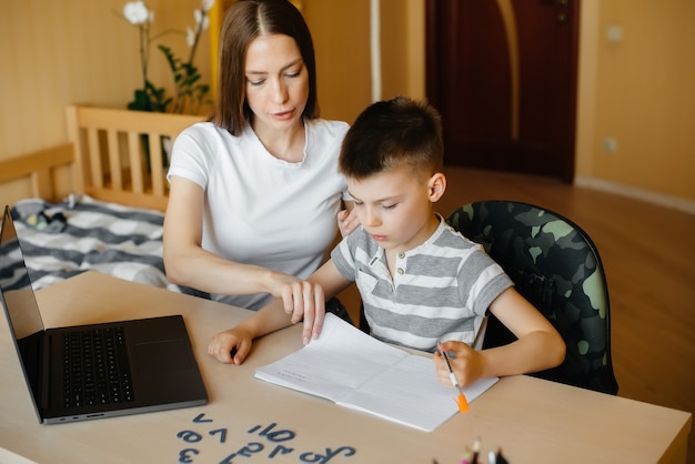 Une mère et son enfant suivent un enseignement à distance à la maison devant l'ordinateur