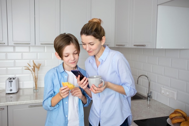 Une mère et son fils adolescent regardent depuis un téléphone portable à la maison dans la cuisine