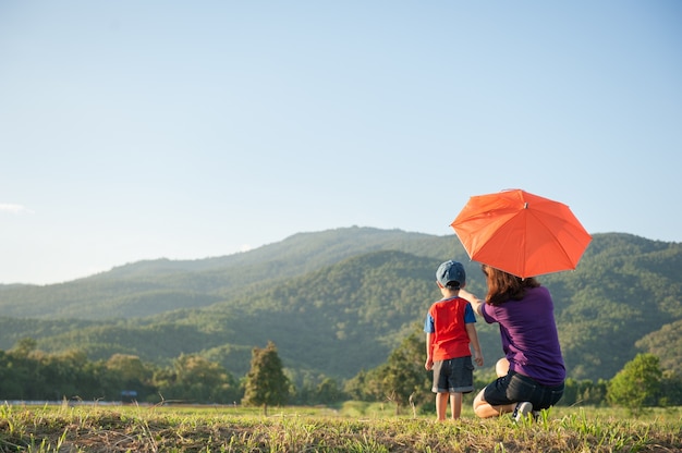 Une mère et son fils tenant un parapluie à l&#39;extérieur au coucher du soleil