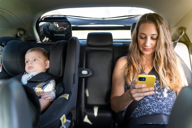 Mère avec son fils voyageant en voiture sur les sièges arrière et utilisant le téléphone