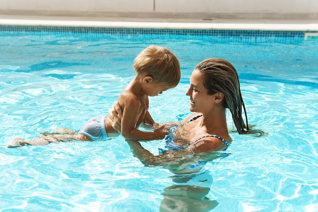 Mère et son mignon petit fils nageant dans une piscine extérieure pendant les vacances d'été