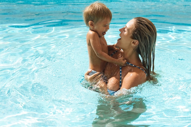 Photo mère et son mignon petit fils nageant dans une piscine extérieure pendant les vacances d'été