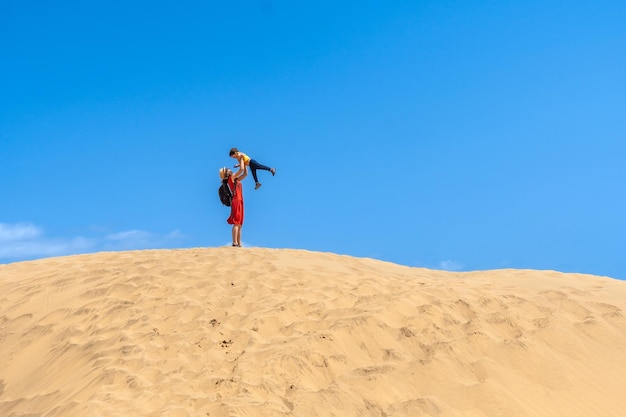 Une mère soulevant un enfant souriant dans les dunes de Maspalomas en été Gran Canarie Îles Canaries