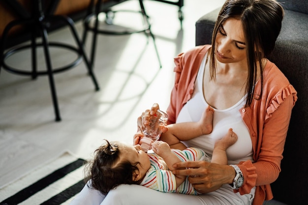 Photo mère souriante nourrissant sa petite fille tout en la tenant sur les genoux à la maison