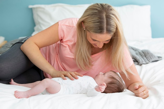 Une mère souriante regardant sa fille nouvellement née sur le lit à la maison.