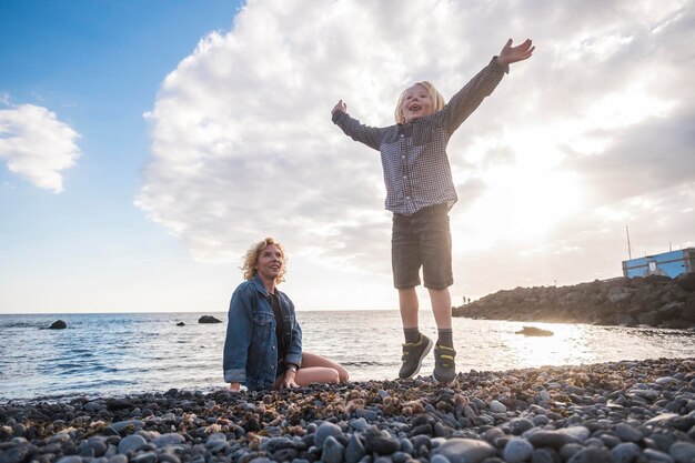 Photo une mère souriante regardant son fils ludique assise face à la mer.