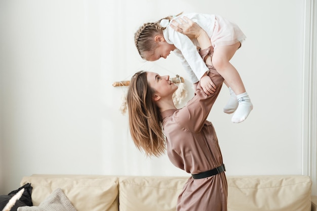 Une mère souriante soulève une petite fille heureuse dans les airs dans le salon et joue avec elle