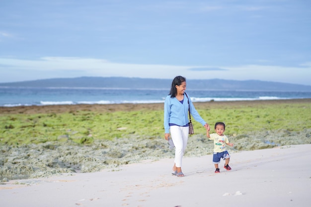 mère tenant la main de l'enfant marchant sur la plage