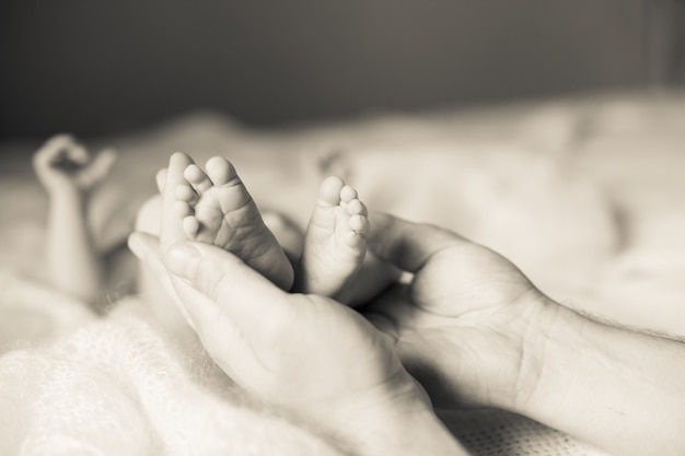 La mère tient dans ses mains les jambes de sa fille nouveau-née. photo dans un style rétro