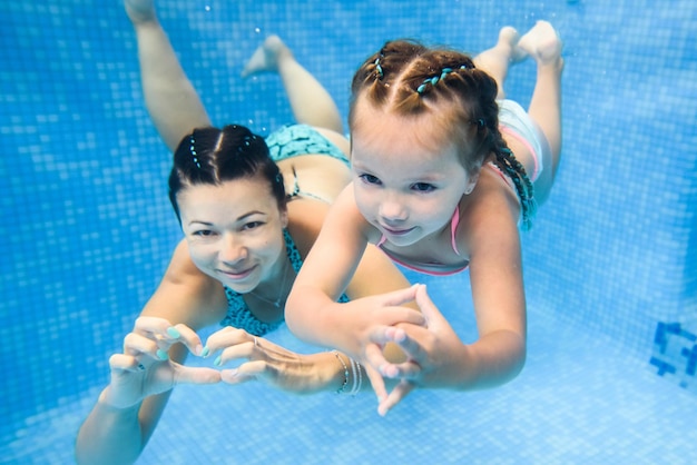 Mère tient sa fille immergée sous l'eau nageant sous l'eau dans la pataugeoire Plongée bébé Apprentissage de la petite fille à nager Enseigne à l'enfant en bas âge à nager