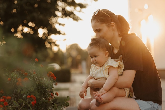 La mère tient sa petite fille sur ses genoux près du buisson de fleurs dans le jardin