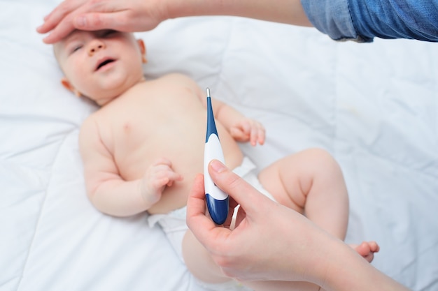 La mère tient un thermomètre dans une main et de l'autre, essaie le front du bébé. Les maladies des enfants.