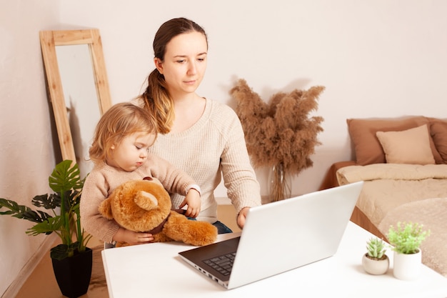 Mère travaille à la maison pour un ordinateur portable l'enfant empêche le travail une jeune femme est indépendante avec elle