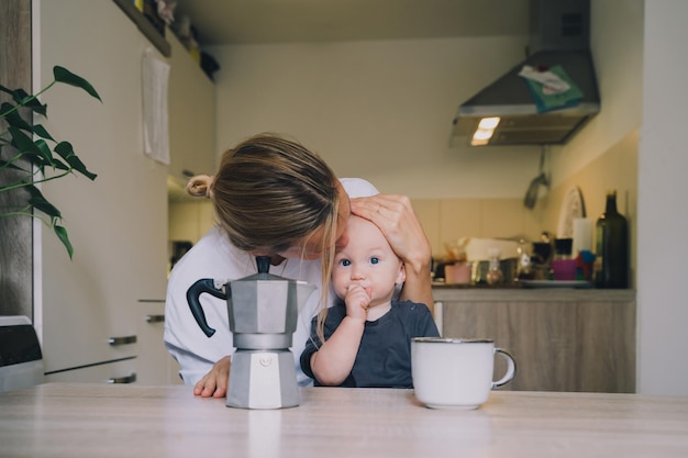 Une mère travailleuse avec un petit bébé, une jeune femme fatiguée avec du café et un bébé prenant le petit déjeuner dans la cuisine.