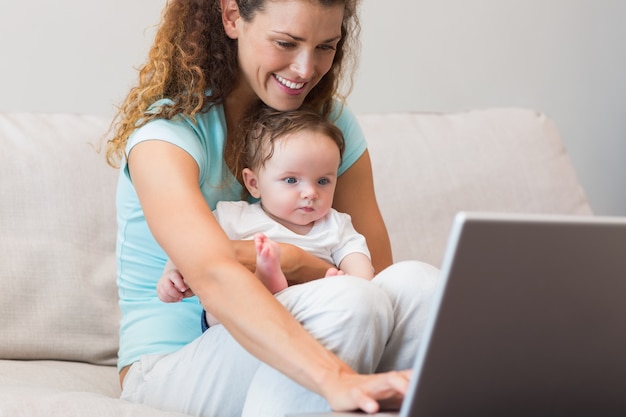 Mère utilisant un ordinateur portable tout en tenant bébé