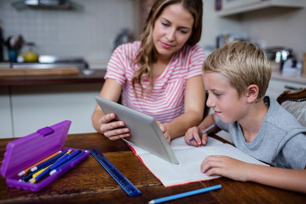 Mère utilisant une tablette numérique tout en aidant son fils à faire ses devoirs