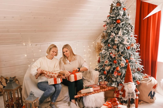 Des mères heureuses se préparent pour Noël, des cadeaux de nouvel an à la maison tout en étant assises près de l'arbre de Noël. Vacances d'hiver, concept de décoration d'intérieur