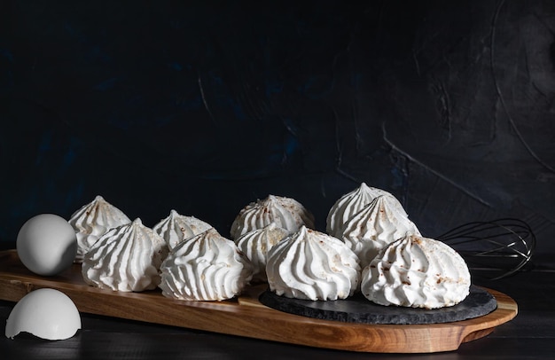 Meringue et coquille d'oeuf sur planche de bois sur fond sombre low kay selective focus Meringue sucrée dessert délicieux et léger Nature morte dans le style de la nourriture