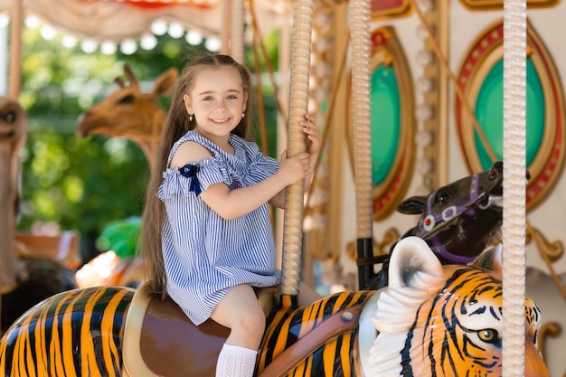 Merrygoround jolie petite fille en robe bleue jouant sur le carrousel au parc d'attractions