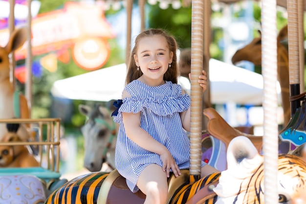 Merrygoround jolie petite fille en robe bleue jouant sur le carrousel au parc d'attractions