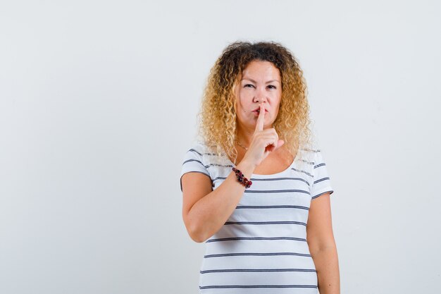 Merveilleuse Dame Montrant Un Geste De Silence En T-shirt Rayé Et Semblant Perturbée, Vue De Face.