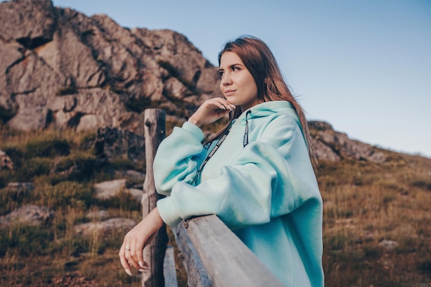 Une merveilleuse jeune femme vêtue d'un sweat à capuche bleu qui regarde une fascinante montagne spacieuse
