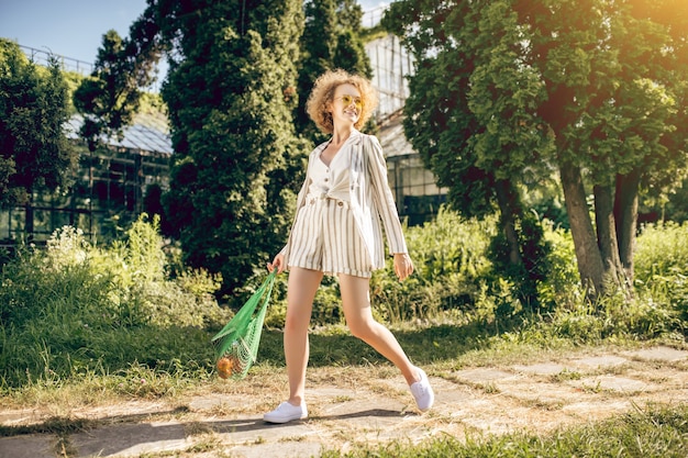 Merveilleuse journée. Jeune femme aux cheveux bouclés marchant au soleil